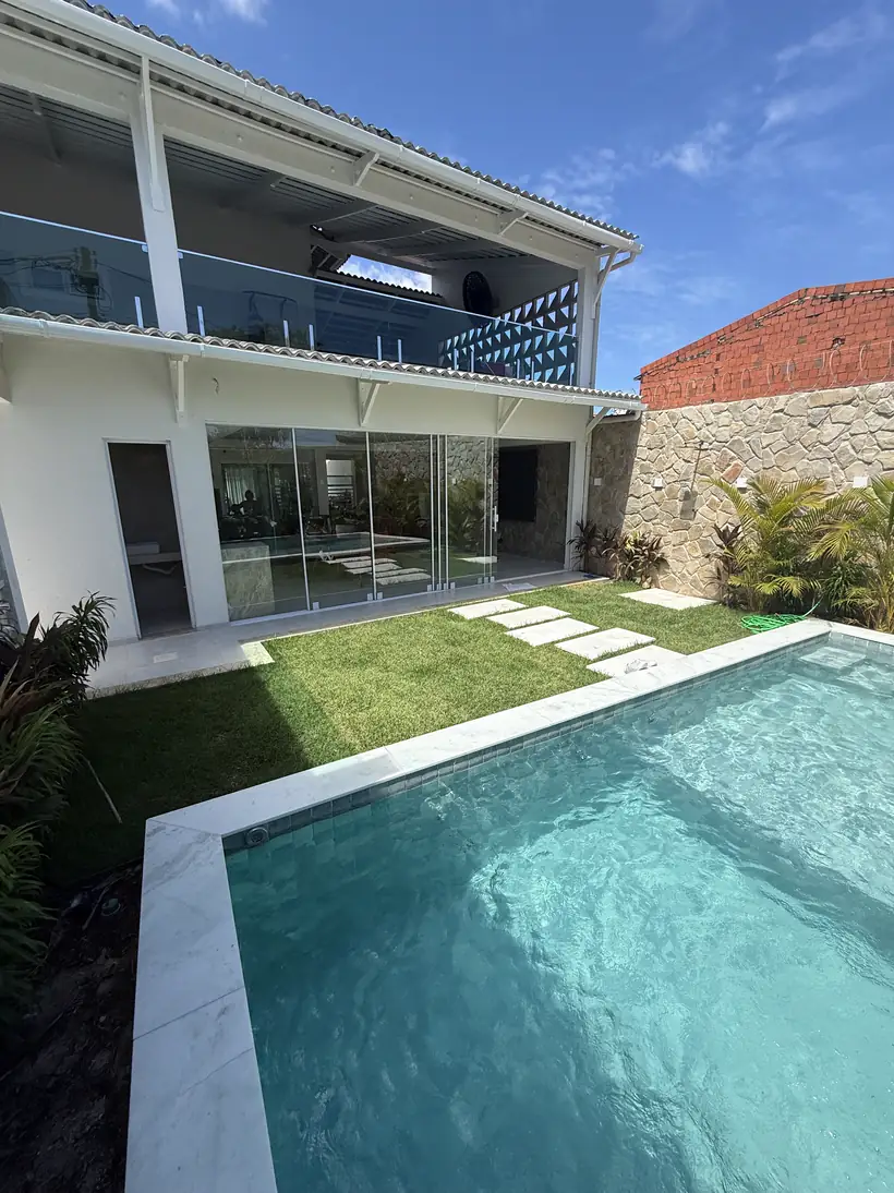 Piscina, gramado e a casa com varanda de vidro no andar de cima